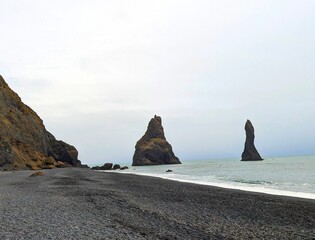 Posągi z czarnej skały wystające z morza obok czarnej plaży  © Asnyko