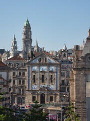 Obraz premium Iconic Porto skyline featuring the Clérigos Tower towering above the Azulejo-clad facade of the São Bento Train Station and surrounding historic buildings.