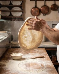 Fototapeta premium Hands stretching fresh pizza dough above a floured work surface in warm kitchen light with copy space, ideal for pizzeria, baking, and artisan food marketing 