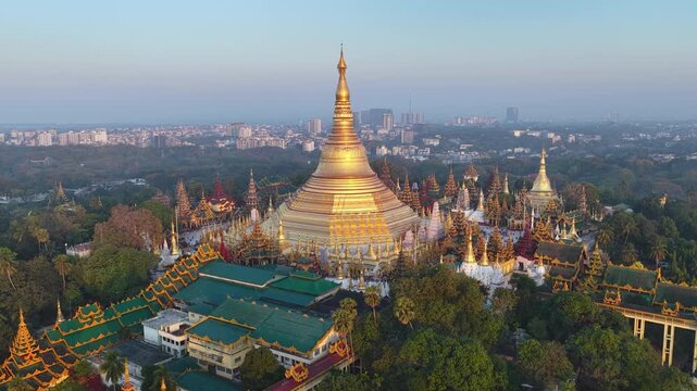 Aerial drone view at Shwedagon Pagoda, a golden stupa, surrounded by lush greenery and urban development in Yangon (Rangun), Myanmar (Burma), showcasing the city's blend of religious and modern life.