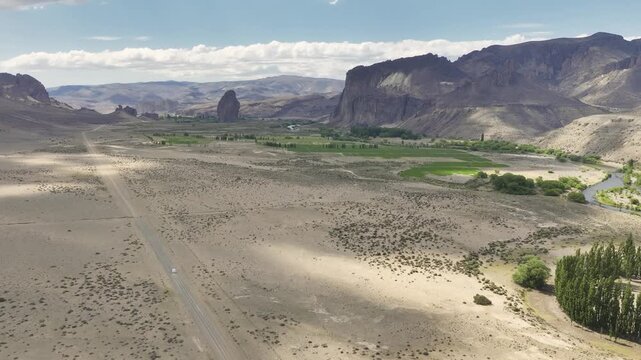 Aerial view of motorhome driving along a rural road through the Patagonian steppe toward the Piedra Parada rock formation in Chubut, Argentina