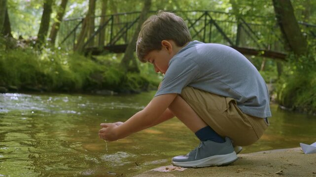 Boy Hands Touching River Flow. Child crouching by sparkling creek, touching cool water in forest. Boy crouches by creek, dipping their hands into cool, flowing water. Relax Refresh Peaceful in Nature.
