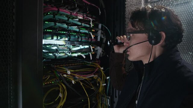 Medium close up shot of network engineer using handheld flashlight to inspect cables and ports inside server rack in modern data center during infrastructure maintenance