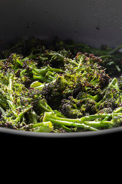 Purple sprouting broccoli frying in a deep ceramic frying pan background backdrop.