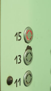 Vertical video person hand pressing the glowing red button for the fifteenth floor on an elevator control panel, preparing to travel upwards in the building