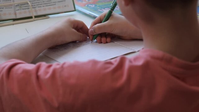 Young students hands writing with a pencil in a lined notebook, studying from a textbook at a desk during class or homework, focused on learning and developing skills