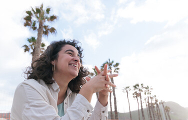 Fototapeta premium A dark-haired girl with curly hair smiles happily at sunset in an outdoor area with palm trees.