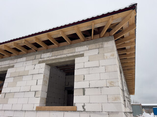 Fototapeta premium Unfinished house building process showing aerated concrete block wall and wooden roof trusses, construction site work