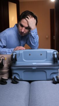 Vertical video man looking frustrated and stressed while trying to pack too many items into an overstuffed suitcase, preparing for a trip or dealing with the challenges of travel preparations