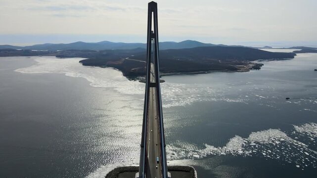 Cars driving across the bridge. View of traffic moving along the cable-stayed bridge connecting island with the mainland. Sea below partially covered with ice. Russky Bridge, Vladivostok, Russia