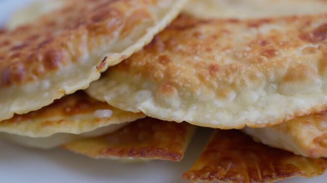 Golden fried chebureki on plate stacked closeup showing blistered browned crust flaky edges oil sheen savory meat filling hint rustic homemade presentation warm snack