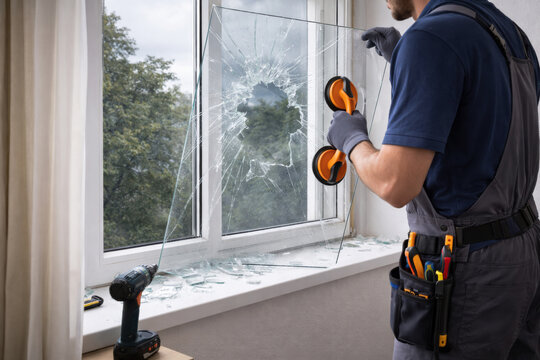 Professional repair technician removing shattered window glass using suction handles during home window replacement. Concept of repair service, maintenance work, and property restoration.