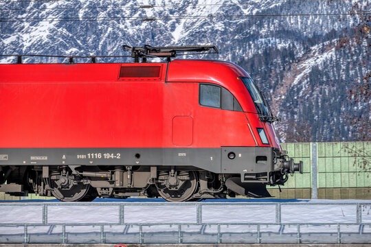 red electric locomotive taurus in front of snow covered alpine mountains, modern railway transport and logistics in austria, close up of train engine with mountain landscape background