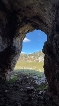 Looking out from the dark cave, one can see a window, an entrance door, and a view of the plateau.