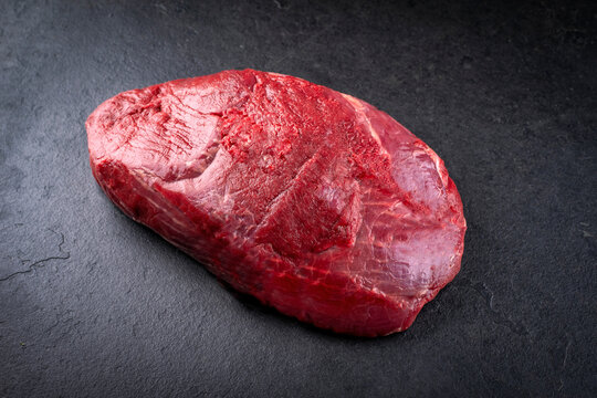 Boneless venison haunch - top round steak raw offered as close-up on a design slate plate