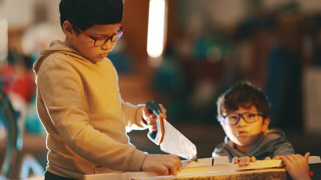 Young boy learning carpentry cutting wood plank with handsaw