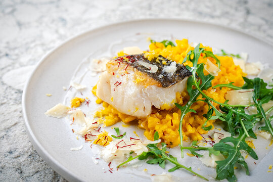 Italian risotto allo zafferano traditional saffron risotto with cod skei fish fillet, parmesan and arugula served as close-up on a design plate