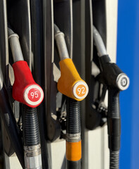 Closeup gas pump nozzles lined vertically, worn plastic handles with red yellow and black caps, coiled hoses and metal dispenser © vipvn