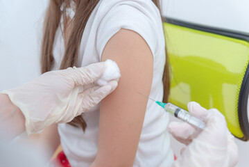 Doctor disinfecting child shoulder with cotton before vaccine injection during pediatric clinic visit, concept of vaccination safety and preventive healthcare