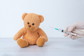 Doctor hand holding syringe near teddy bear toy representing vaccination concept for children,...