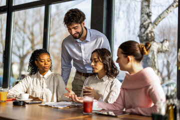 Fototapeta na wymiar Male colleague standing and working with three female partners at a restaurant table.