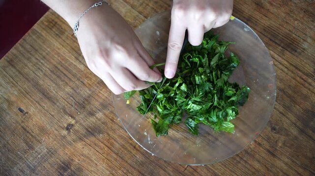 Chef cutting fresh parsley and basil in a bowl