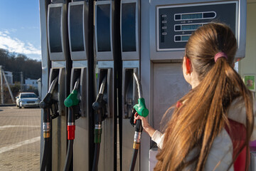 Woman refueling car at gas station pump. Close-up of a woman holding a fuel nozzle at a gas station pump, showing car refueling, transport costs, and everyday driving. © Iryna