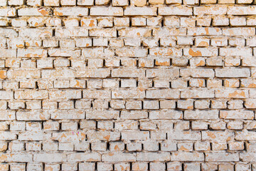 Obraz premium Old white brick wall with peeling paint. Close-up of a weathered brick wall covered with cracked white paint, showing aged texture, rough masonry, and rustic urban character.