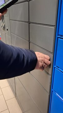 Man places white parcel into secure locker at postamat station. Simple process of shipping packages via automated terminals. Efficient logistics, trend of contactless shipping services for e-commerce