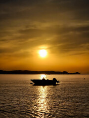 Boat silhouette on calm sea at golden sunset with reflection on water