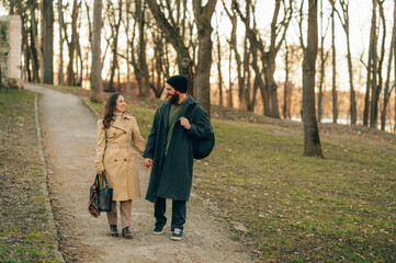 Fototapeta premium Couple Walking In Autumn Park Path, Two People Wearing Coats And Backpacks Sharing Conversation