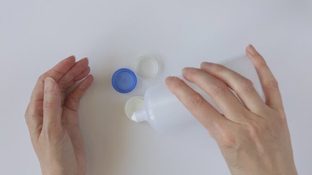 Woman pouring contact lens solution into a contact lens case against a white background. The woman's hands are holding the contact lens case. Conceptual image of eye care and hygienic lens storage.
