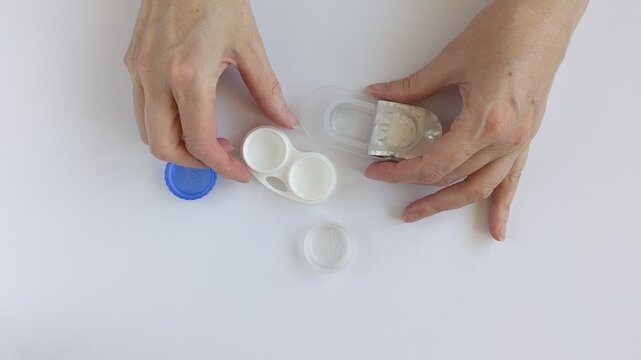 Woman hands place a new contact lens into a container with contact lens solution. Hands remove a contact lens from open plastic blister pack. Eye care and hygiene when wearing contact lenses.