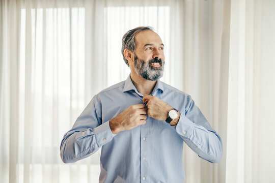 Confident mature man buttoning shirt getting dressed for success