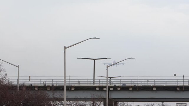 A giant white 4 engine airplane coming in for a landing over a bridge.