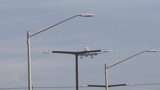 A  white twin-engine airplane coming in for a landing over a bridge and street lights.