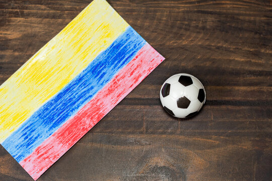 Child's drawing of the Colombian flag next to a soccer ball on a wooden table, concept of soccer passion and Colombian pride