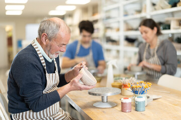 Mature man at table molds cup from wet clay in a pottery workshop