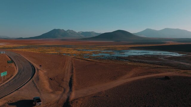 Aerial view of a car traveling through the vast landscapes of northern Chile. Desert plains and volcanic mountains stretch across the horizon.