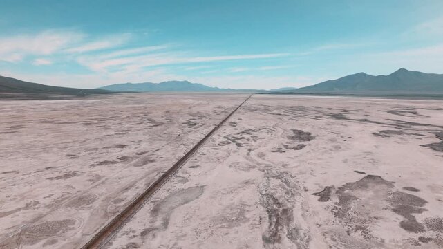 Aerial view of railway tracks stretching across the remote Andean Altiplano. The line cuts through vast high-altitude landscapes beneath volcanic peaks.