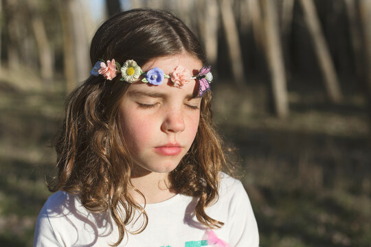 Portrait of a young girl with her eyes closed wearing a floral headband standing in a garden
