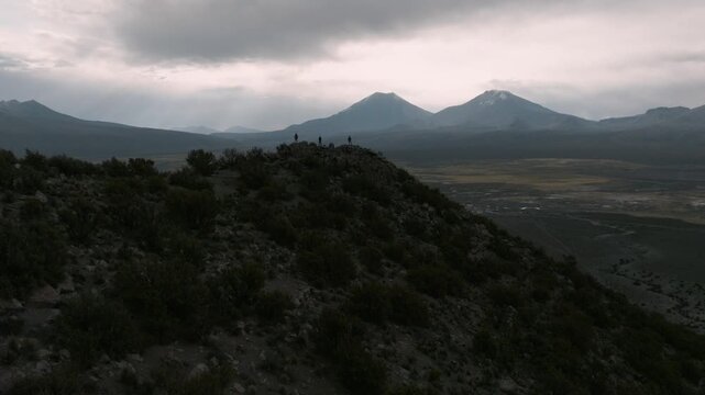 Aerial view of three hikers standing on a mountain ridge near Sajama National Park, surrounded by the vast landscapes of the Bolivian Andes.