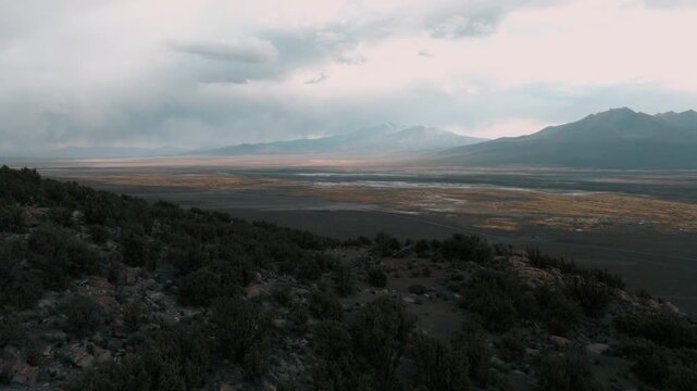 Aerial sunset over Sajama plains in Bolivia, warm golden light illuminating vast Altiplano landscape. Minimalist scenery with long shadows and dramatic sky.