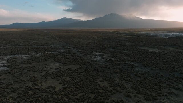 Aerial sunset over Sajama plains in Bolivia, warm golden light illuminating vast Altiplano landscape. Minimalist scenery with long shadows and dramatic sky.