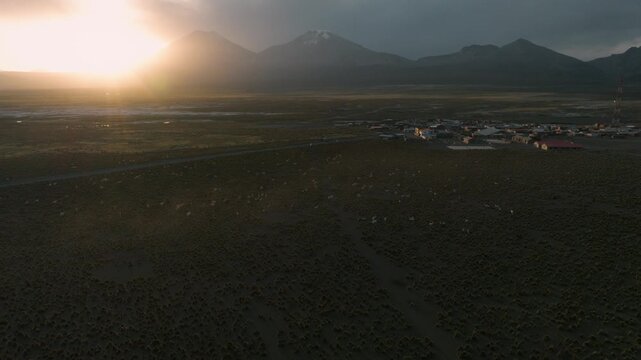 Aerial sunset over Sajama plains in Bolivia, warm golden light illuminating vast Altiplano landscape. Minimalist scenery with long shadows and dramatic sky.