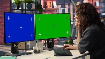 Employee in office working on PC with isolated copy space on dual monitors, creative agency modern setup. Woman focused on graphic design, coding or AI powered tasks in optimized space. Camera B. © DC Studio