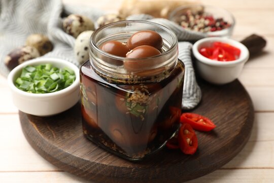 Tasty pickled quail eggs in glass jar and ingredients on light wooden table, closeup