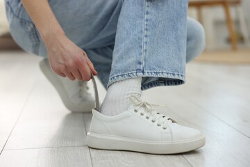 Woman putting on stylish sneakers with shoehorn at home, closeup