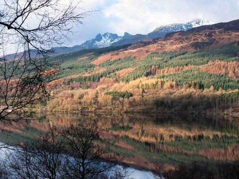 Ben Arthur, better known as The Cobbler, seen from the West Highland Way on the east bank of Loch Lomond with mirror-like reflections of the autumn colours in the calm water.