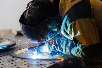 Close-up shot of a welder in safety mask arc-welding steel parts